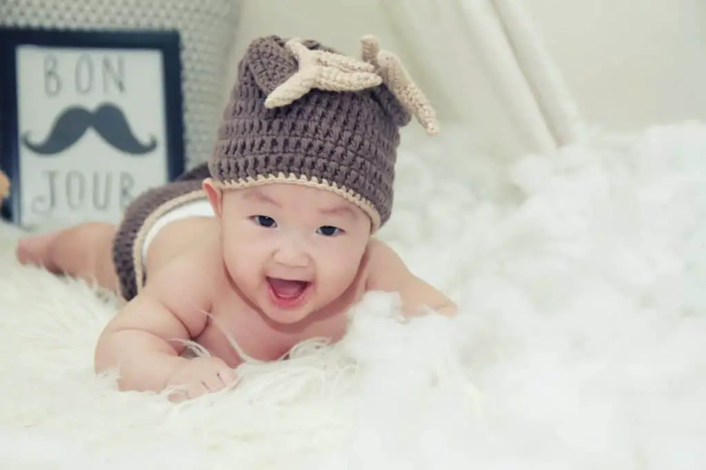 Chinese baby with a heat is crawling on a white rug 