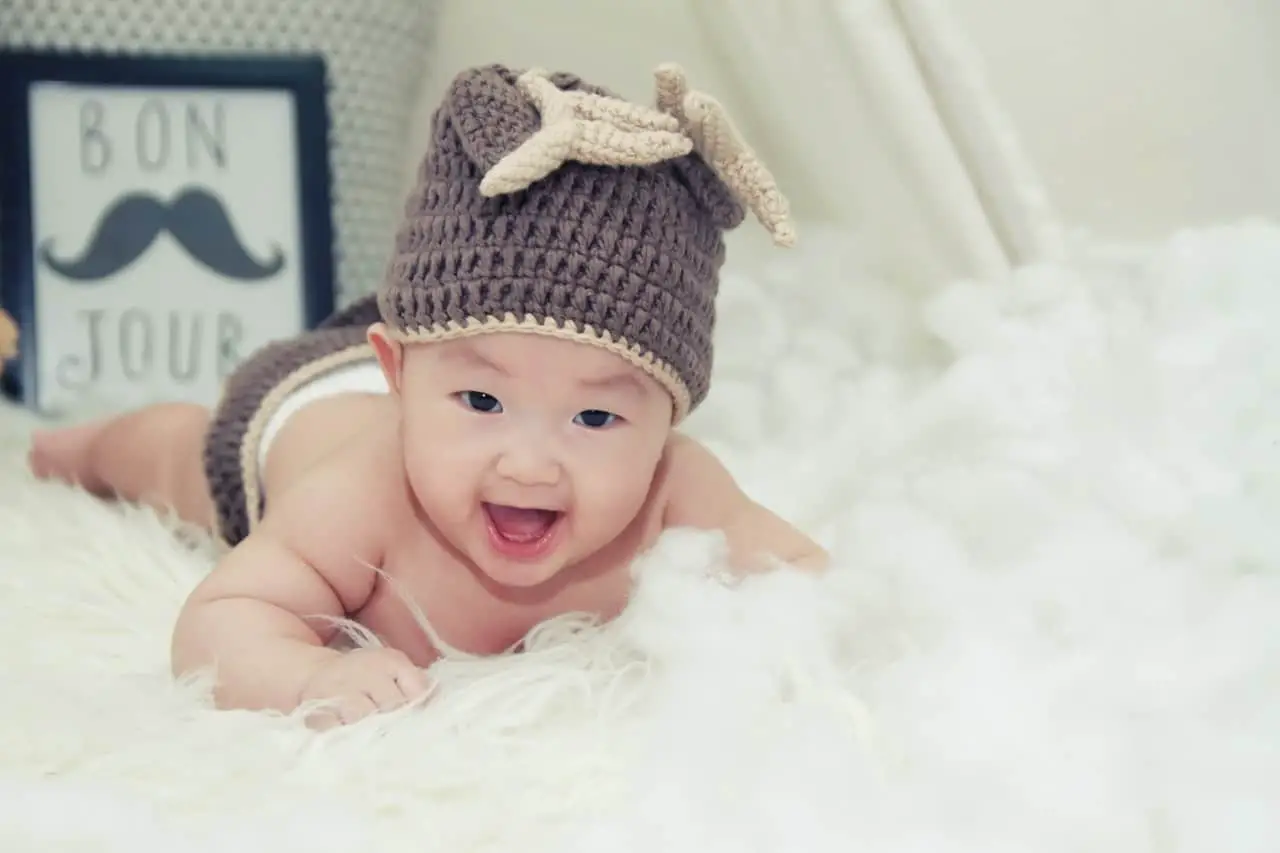 Chinese baby with a heat is crawling on a white rug