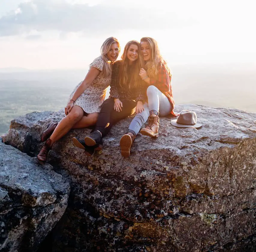 three girls are sitting on a rock and smiling
