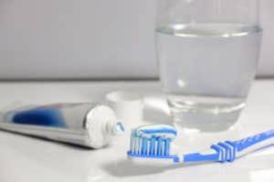 toothpaste is put on toothbrush and a glass of water is nearby