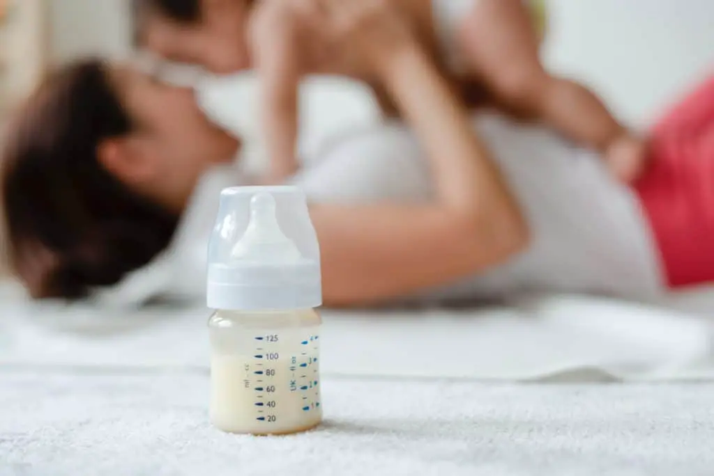 breastmilk bottle with mother and baby in the background
